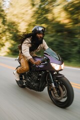 Obraz premium Man leaning forward riding cafe racer motorcycle on winding road