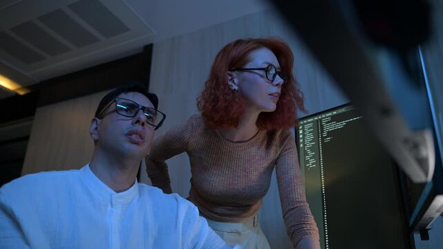 Two software developers collaborating at night, focusing on code review and debugging process on a computer screen, representing teamwork, innovation, and modern software development workflow.
