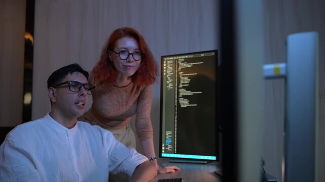 Two software developers collaborating at night, focusing on code review and debugging process on a computer screen, representing teamwork, innovation, and modern software development workflow.