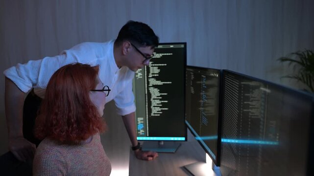Two software developers collaborating at night, focusing on code review and debugging process on a computer screen, representing teamwork, innovation, and modern software development workflow.