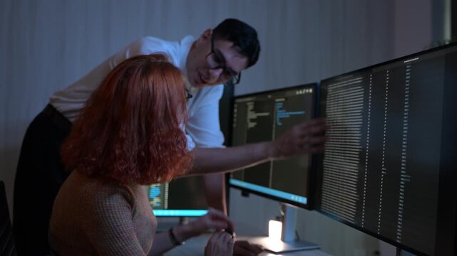 Two software developers collaborating at night, focusing on code review and debugging process on a computer screen, representing teamwork, innovation, and modern software development workflow.