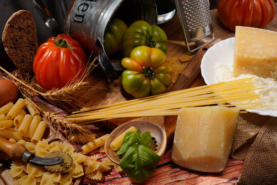 Still life, natura morta con pomodori su tavola imbandita con scenografia di vasi, pentole, utensili, calice di vino e brocca
