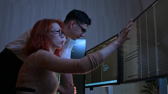 Two software developers collaborating at night, focusing on code review and debugging process on a computer screen, representing teamwork, innovation, and modern software development workflow.