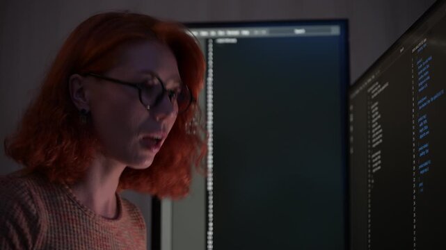 Focused female software developer coding at night in a modern workspace, wearing glasses and analyzing code on computer screen. Concept of programming, technology, cybersecurity, and digital innovatio