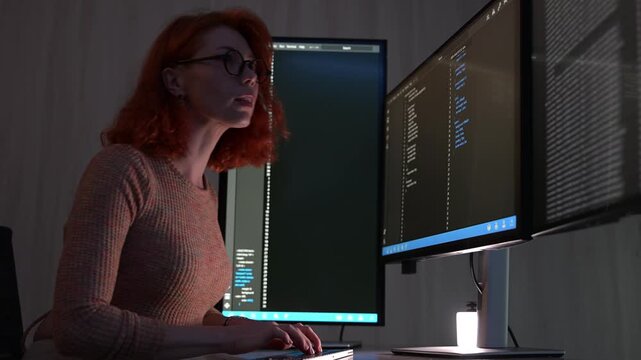 Focused female software developer coding at night in a modern workspace, wearing glasses and analyzing code on computer screen. Concept of programming, technology, cybersecurity, and digital innovatio