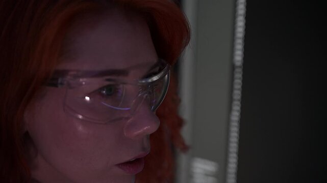 Focused female software developer coding at night in a modern workspace, wearing glasses and analyzing code on computer screen. Concept of programming, technology, cybersecurity, and digital innovatio