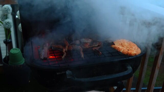 Grilled meat and flatbread on smoky outdoor barbecue grill. Thick white smoke rising from a black grill with meat and pita bread on top.