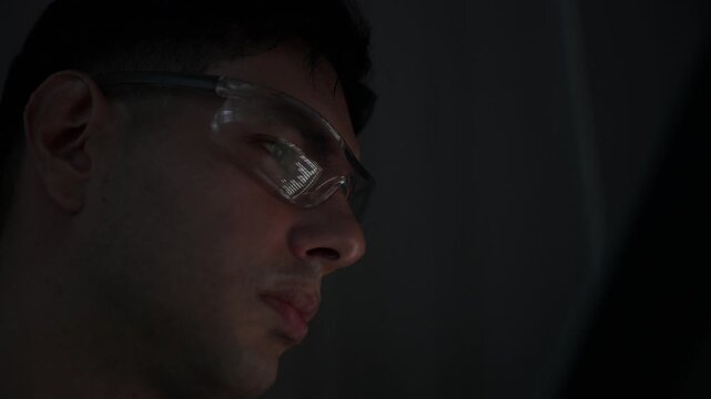 Focused young female software developer programming code on multiple monitors in a dark home office at night. Professional woman engineer working on cyber security and data science tech project.