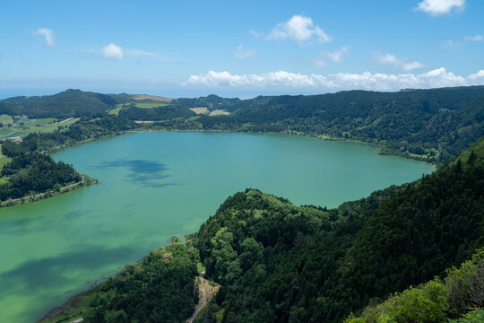 Aerial view of an emerald crater lake surrounded by dense forested caldera and rolling hills, showcasing the volcanic beauty and serenity of Sao Miguel, Azores, Portugal.