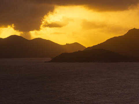 Aerial view of silhouetted tropical islands and mountains under a dramatic golden sunset sky with heavy clouds Anse Reunion, La Digue, Seychelles.