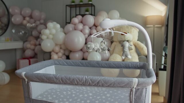 Neutral colored baby crib with star pattern mattress and hanging mobile featuring plush animals, set against a backdrop of pastel balloons and a large teddy bear