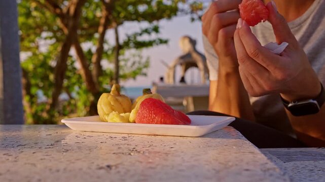 Close Up of Hand Picking Juicy Pomelo Slice from Plate with Tropical Fruit at Seaside Table in Warm Golden Light, Healthy Snack Lifestyle