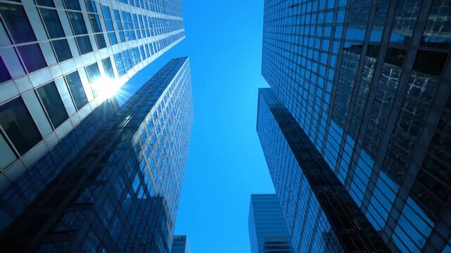 Low-angle shot of multiple modern skyscrapers reaching towards a bright, cloudless sky