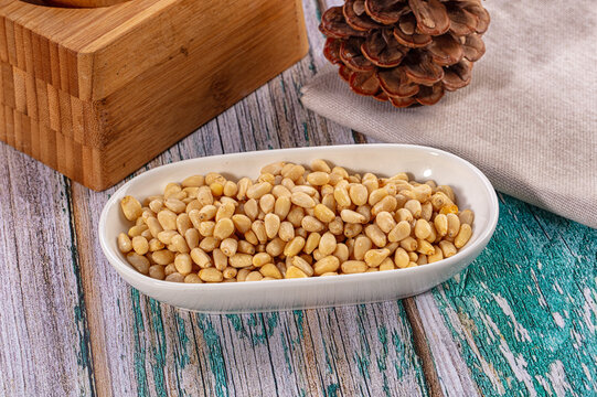 Shelled pine nuts in a white bowl on a rustic teal and brown wooden table