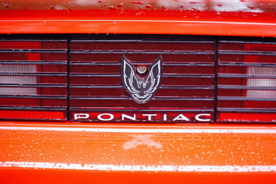 An orange red Pontiac Firebird, rear end featuring the Pontiac logo and crest. Raindrops on the red paint in Hanover, Germany.
