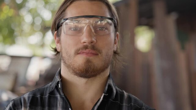 Portrait of a confident male carpenter wearing safety goggles in a carpentry workshop. Serious professional craftsman posing in his woodworking studi