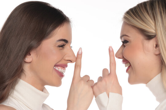 Studio shot of two young women side view portrait smiling and making playful shh silence gesture on a white background