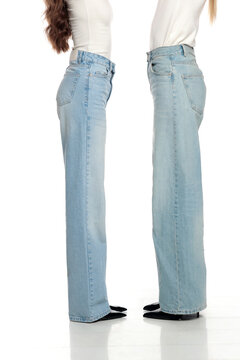 Studio shot of two young women in white tops and denim jeans standing side view on a white background