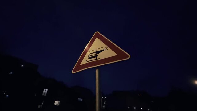 Unusual road sign warning of a nearby helipad or low-flying helicopters, with rain drops falling on the camera lens during a dark and mysterious night in the city