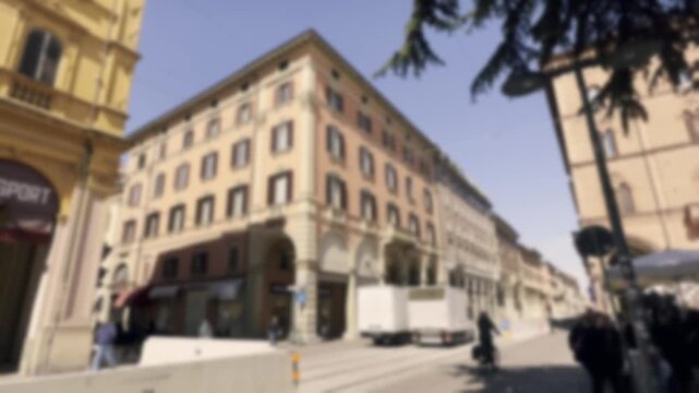 Anonymous crowd and traffic moving through a sunlit, blurred street in a historic European city center, with classic architecture and a soft focus creating an atmospheric, out-of-focus bokeh effect
