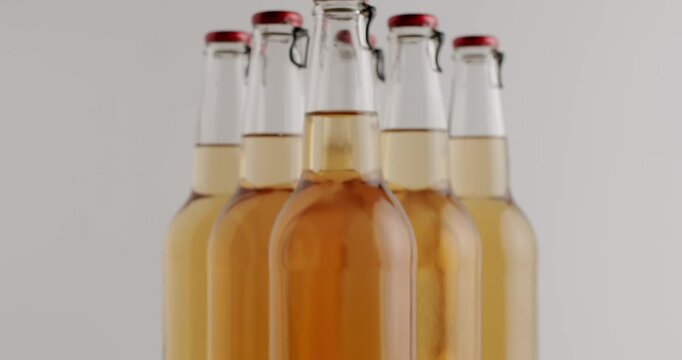 Several swing-top bottles filled with golden craft beer rotating on a surface with wheat ears and barley grains. Light reflects off the clear glass showing the different colors of the beverage