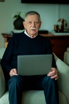 Senior man sittting in a comfortable armchair and using a notebook