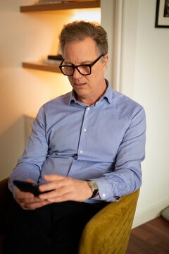 Mid aged man with cellphone on his hand sitting in a chair at home
