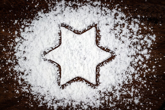 Sugar powder forms a star shape on a wooden surface in a kitchen during baking preparations
