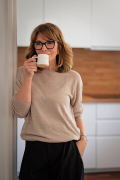 Confident blond haired woman standing in her modern home and drinking a coffee