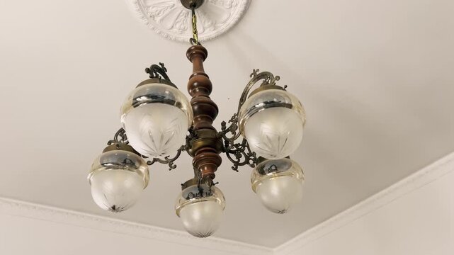 Elegant vintage chandelier with a wooden body and five art nouveau style glass lampshades hanging from an ornate ceiling with a decorative rosette, creating a luxurious and classic atmosphere