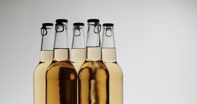 Clear glass bottles with swing top caps filled with a refreshing golden beverage, possibly craft beer or cider, moving together in slow motion on a clean, isolated white background