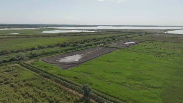 Aerial view of Camargue France with vast green wetlands marshes and large dark mudflat pond under bright blue sky with distant water and horizon