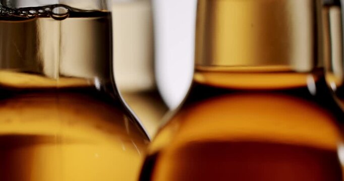 Detailed macro shot of amber glass beer bottles moving in slow motion along a production line in a brewery, with the liquid and bubbles visible against a bright white background
