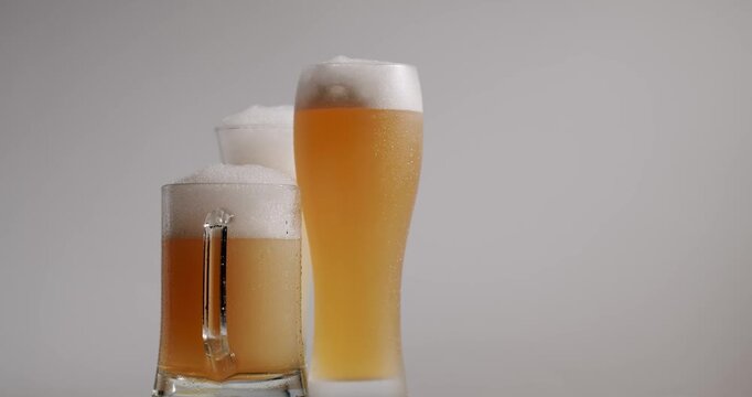 Three rotating glasses of fresh, cold lager and wheat beer with a lot of foam isolated on a white background. Delicious frosty beverage for a pub party or celebration in slow motion