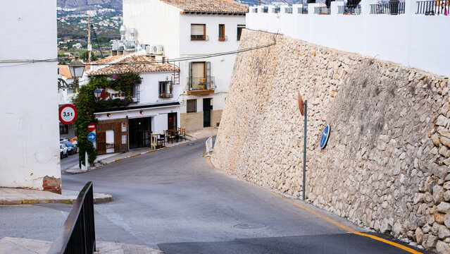 Altea, Spain - November 02, 2025: Narrow street in Spanish village with whitewashed buildings and stone wall, road signs visible on the side