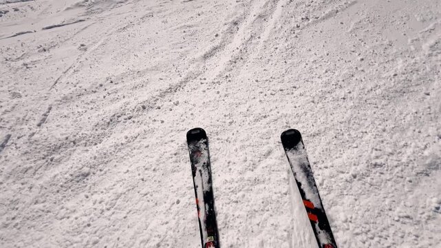 Point of view shot of a skier starting to slide down a mountain slope, with skis carving through the fresh snow and the skier's shadow cast on the white surface on a sunny winter day