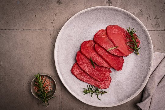 Raw sliced beef or lamb tenderloin meat, beef steaks on plate with spices for cooking on gray background, top view
