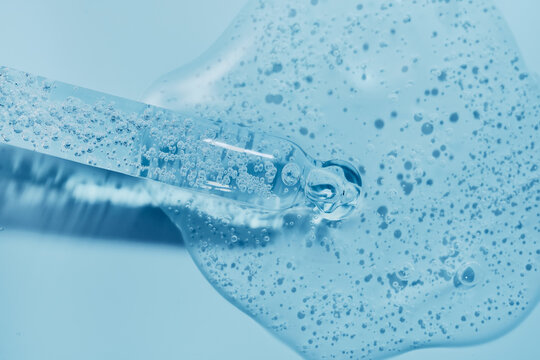 Clear liquid serum with bubbles flowing from dropper on blue background