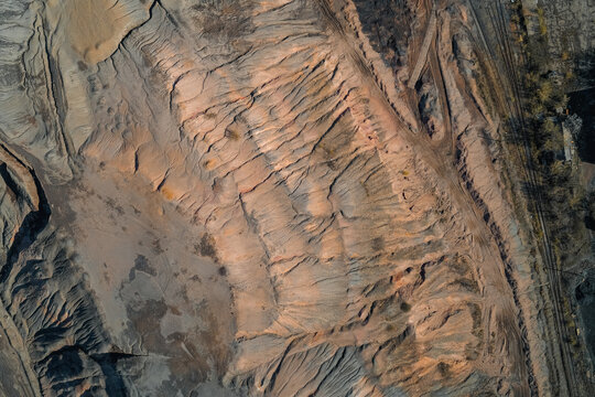 Eroded surface of industrial slag heap with deep canyons and orange mineral soil textures in open pit mining area, aerial drone view from above