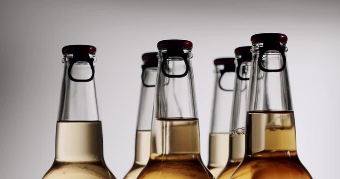 Slow motion footage showing the liquid level in a row of glass bottles with swing top caps mysteriously decreasing, Glass bottles full of light and dark beer slowly rotating in a studio setting