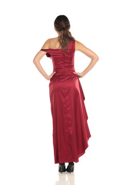 Studio shot of a brunette woman in a red evening gown standing full length rear view on a white background