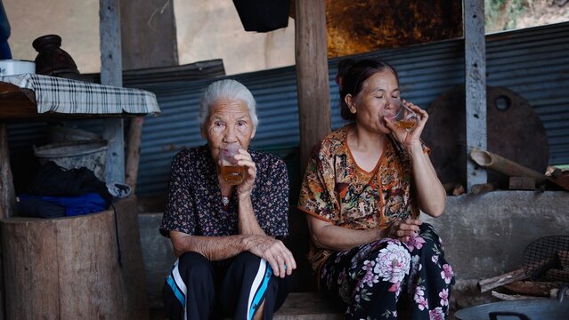 Two elderly women are sitting in their traditional home, savoring a moment of tranquility as they drink tea