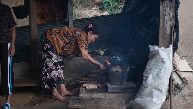 Mature woman managing wood burning stove, preparing meal in vintage kitchen with traditional cooking equipment