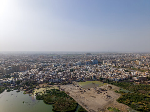 Aerial view of the sprawling urban landscape with dense residential buildings, green wetlands, and a hazy horizon in Hyderabad, Sindh, Pakistan.