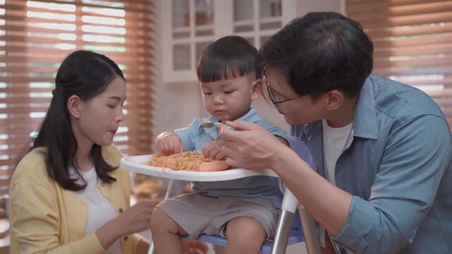 Playful toddler feeding spaghetti to mother during mealtime, happy family interaction, messy eating learning, love bonding and home lifestyle concept