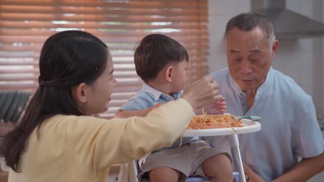 Cute toddler playing with spaghetti during mealtime, happy parents encouraging self feeding, messy eating learning, family lifestyle and child development concept
