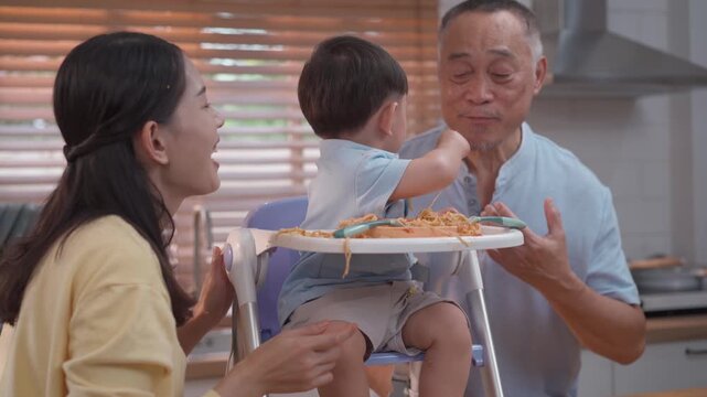 Cute toddler playing with spaghetti during mealtime, happy parents encouraging self feeding, messy eating learning, family lifestyle and child development concept