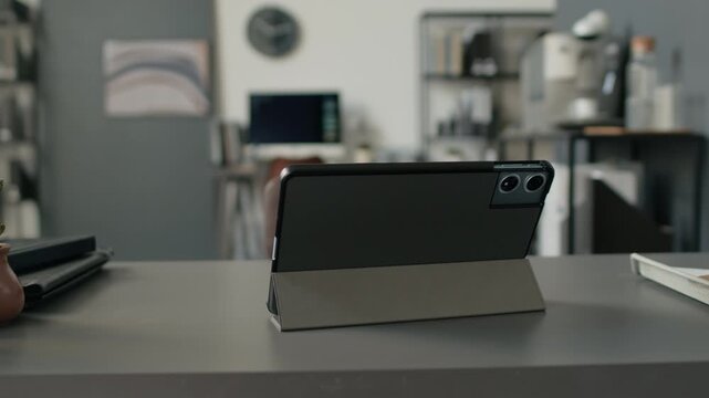 Low angle close up no people shot of digital tablet on stand with notebooks on table in modern minimalist office