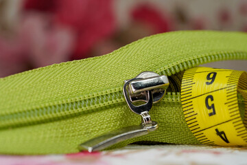 Macro shot of a green zipper with a yellow measuring tape on fabric background. Ideal for concepts related to tailoring, fashion design, clothing production, and DIY sewing projects © aykutkarahan