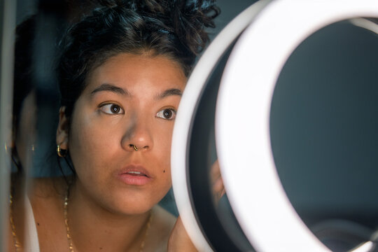 Young woman applying makeup looking into ring light